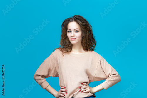 Portrait of a young beautiful woman wearing sweatshirt holding hands on hips isolated over blue background