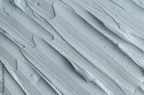 Gray bentonite facial clay (mask, face cream, body wrap) texture close up, selective focus. Abstract background with brush strokes.