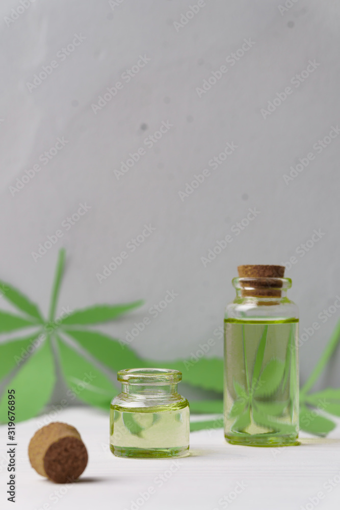 Hemp oil in two small glass bottles and leaves on a light concrete surface. Image contains copy space, vertical orientation. The concept of natural medicine and body care. Hemp oil in two small glass bottles and leaves on a light concrete surface. Image contains copy space, vertical orientation. The concept of natural medicine and body care.