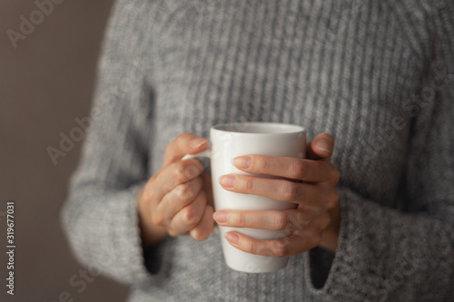A girl in a sweater holds a white mug.