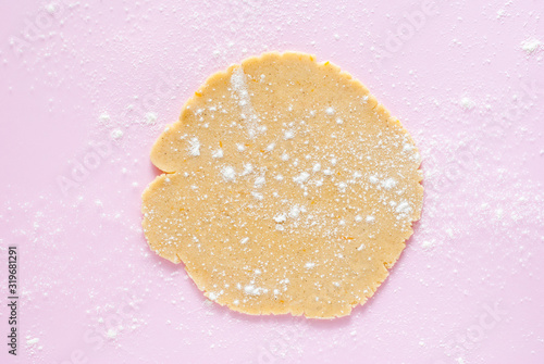 Rolled into a round dough for sugar cookies sprinkled with flour on a pastel pale pink background. Bright backdrop with texture.