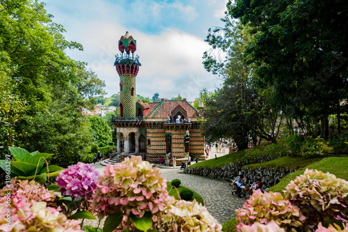 Fotografie Capricho de gaudí con flores por abajo dia claro con nubes