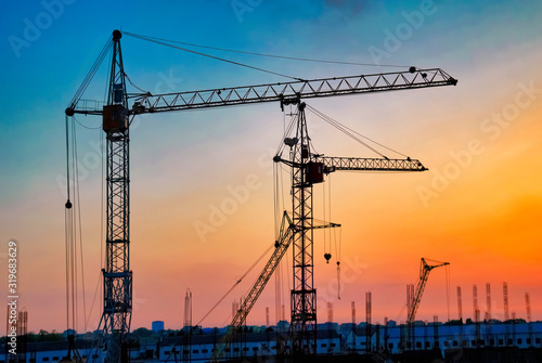 Industrial landscape with silhouettes of cranes on the sunset background