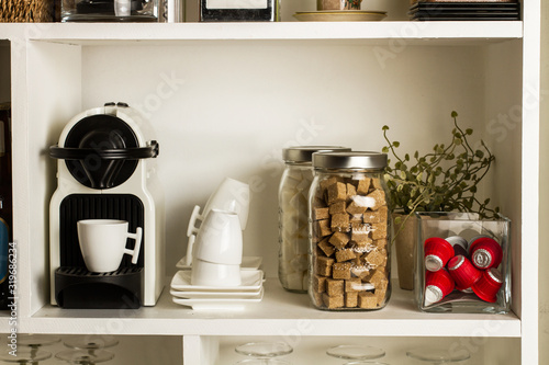 Cafetera automática con tazas de café, azúcar en terrones en una biblioteca sobre estantes blancos Vista de frente photo