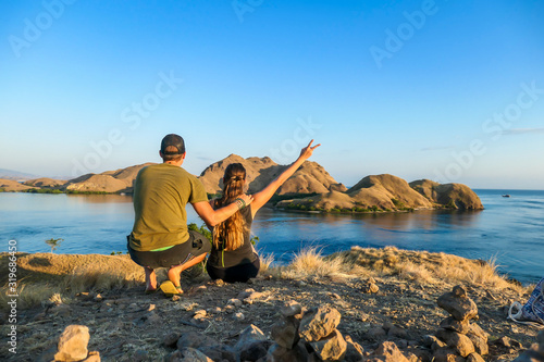 A couple sitting on top of a small island, enjoying the morning sun over Komodo National Park, Flores, Indonesia. Golden hour over the islands and sea. They are enjoying their time. Love and happiness
