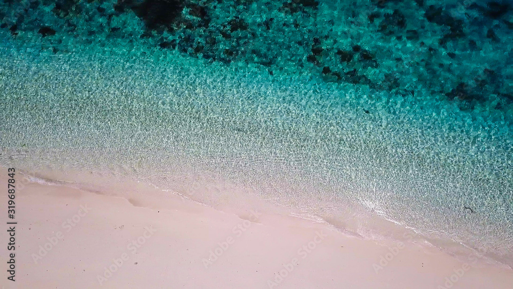 Fototapeta premium A drone shot of a pink sand beach on a small island near Maumere, Indonesia. Happy and careless moments. Waves gently washing the shore.Clear, turquoise coloured water displaying coral reef.