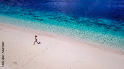 A drone shot of a girl playing on the beach on a small island near Maumere, Indonesia. Happy and careless moments. The coast changes colors from white to turquoise and navy blue. There are few islands