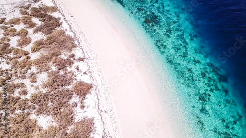A drone shot of a pink sand beach on a small island near Maumere, Indonesia. Happy and careless moments. Waves gently washing the shore.Clear, turquoise coloured water displaying coral reef.