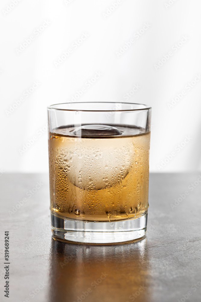 wet glass with strong whiskey and ice cube on white wet glass with strong whiskey and ice cube on white