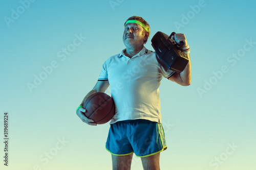 Senior man posing stunning in sportwear with retro tape recorder on gradient background, neon. Caucasian male model in great shape, sportive. Concept of sport, activity, movement, healthy lifestyle. © master1305