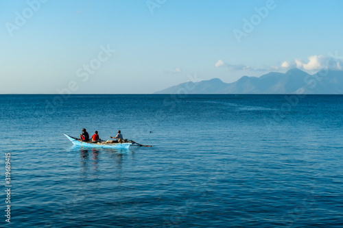Flores/Indonesia 20290808: A fishermen's boat crossing a calm sea near Maumere, Indonesia There are three men in one small, blue boat, one of them is paddling. Calm surface of the sea. photo