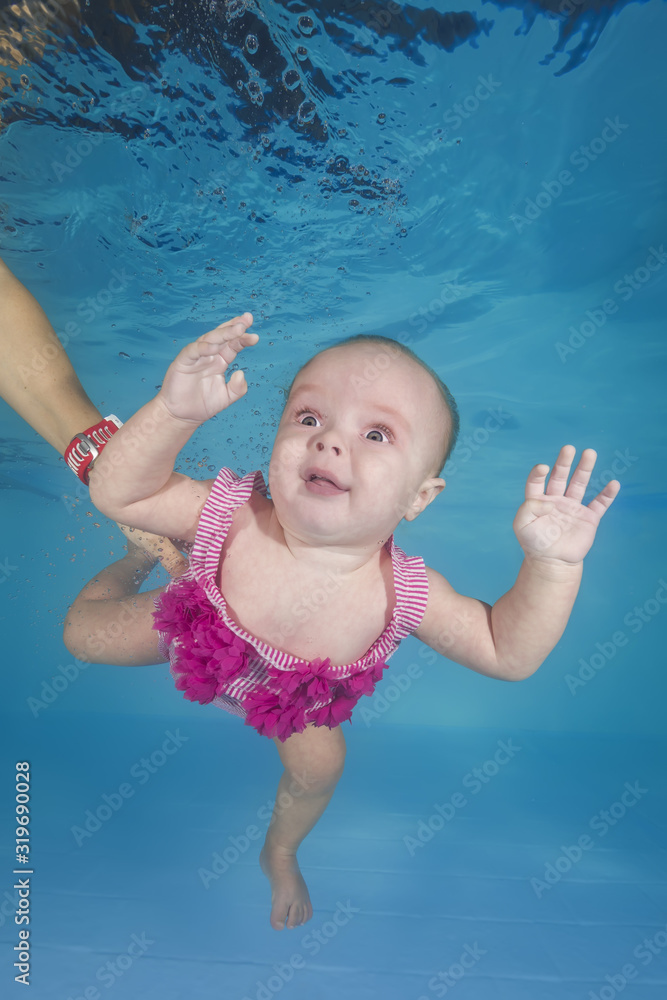 little girl in a pink swimsuit learns to dive underwater in the swimming pool