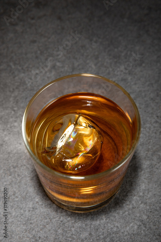 top view of frozen ice cube in glass of brandy on grey surface