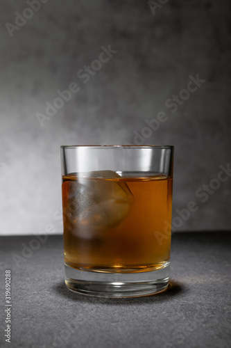 frozen ice cube in glass of whiskey on grey