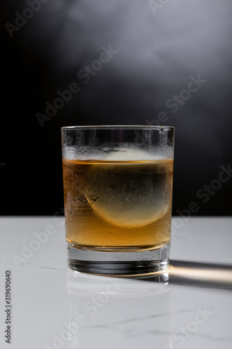 ice cube in glass of whiskey on black with smoke
