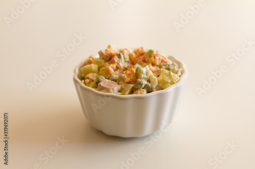 Olivier in a white plate on a pale pink background. the winter salad.ingredients: cucumber, sausage, meat, mayonnaise, sour cream, potatoes, peas, egg. space for your text.