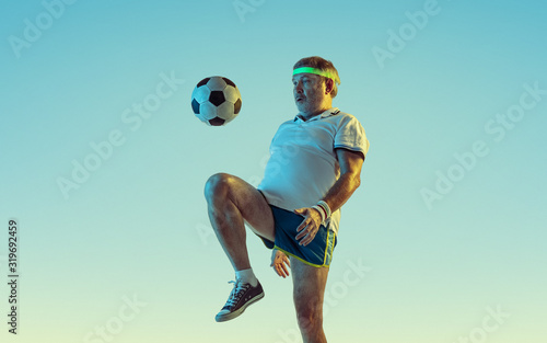 Foto Senior man playing soccer, football on gradient background in neon light