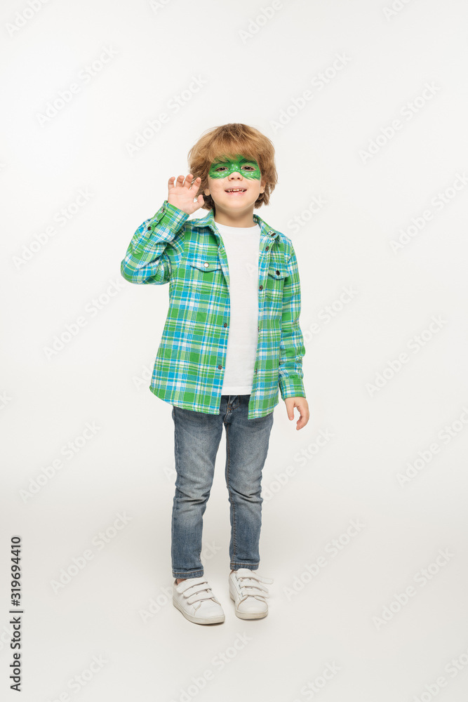 full length view of cute boy with gecko mask painted on face waving hand at camera on white background full length view of cute boy with gecko mask painted on face waving hand at camera on white background