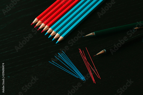 Blue and red pecils, mechanical pencils and pencil lead composition in a black wood background photo