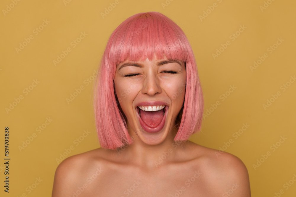 Good looking young cheerful attractive woman with pink bob hairstyle keeping her mouth wide opened while standing over mustard background with closed eyes Good looking young cheerful attractive woman with pink bob hairstyle keeping her mouth wide opened while standing over mustard background with closed eyes