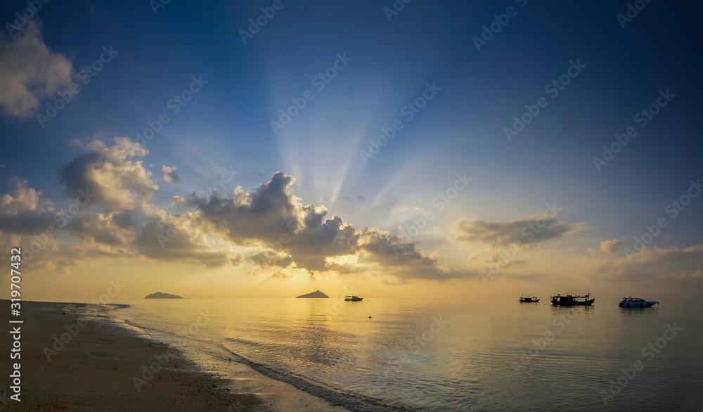 view panorama seaside of small boat floating in the sea with small island and sun rays with yellow sun light and cloudy sky background, sunrise at Ko Bulon Le, Stun Province, southern of Thailand.