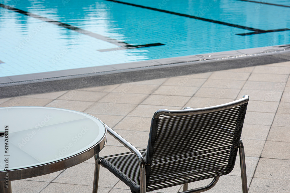Relaxing chair and circle glass table near a swimming pool in a sport club with a relaxing atmosphere waiting for someone to sit on. Holidays, long vacations or short break. Relaxing chair and circle glass table near a swimming pool in a sport club with a relaxing atmosphere waiting for someone to sit on. Holidays, long vacations or short break.