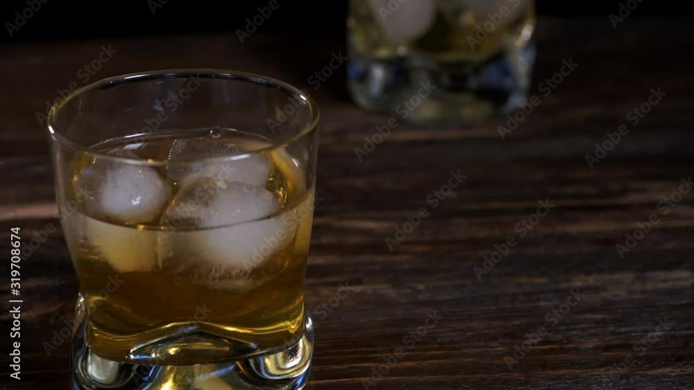 Ice cubes fall into a glass with golden malt whiskey Ice cubes fall into a glass with golden malt whiskey