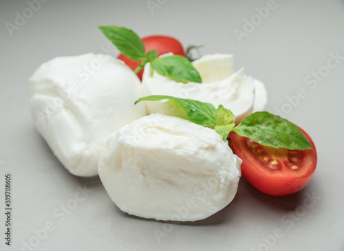 Traditional Italian mozzarella cheese with herbs and tomatoes on gray background.