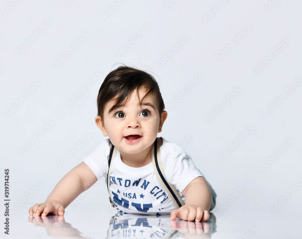 Little toddler in t-shirt with inscriptions, jeans with suspenders. He is laying on floor isolated on white background. Close up Little toddler in t-shirt with inscriptions, jeans with suspenders. He is laying on floor isolated on white background. Close up