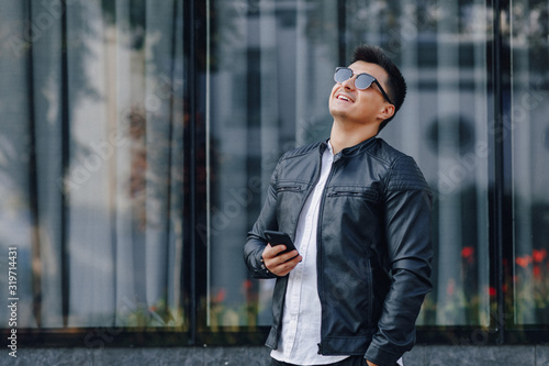 young stylish guy in glasses in black leather jacket with phone on glass background