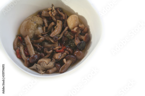 Various type of mushrooms in oil on a white bowl isolated on white background