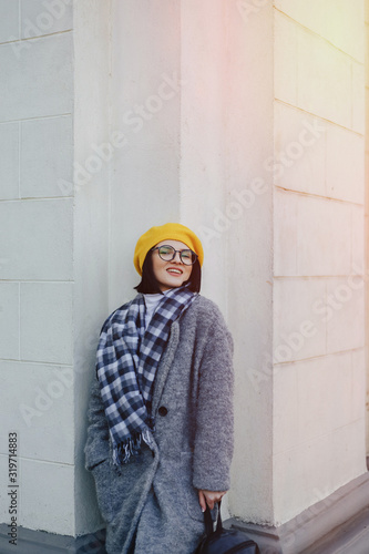 Attractive smiling young girl in glasses in coat and yellow Beret on a simple light background © pressahotkey