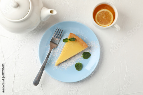 Plate with lemon tart slice, teapot and cup of tea on white background, top view