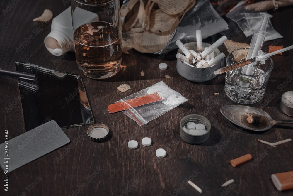 Various drugs, alcohol and cigarettes are on the wooden table. Substances that cause drug and alcohol dependence. Low key. Various drugs, alcohol and cigarettes are on the wooden table. Substances that cause drug and alcohol dependence. Low key.