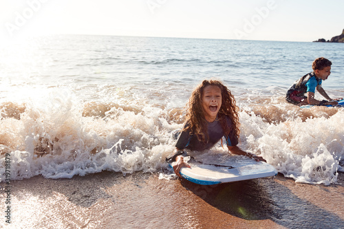 Tableau sur toile Two Children Wearing Wetsuits Playing In Sea With Bodyboards On  Summer Beach Va