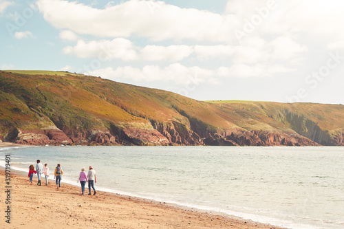 Rear Wide Angle View Of Multi-Generation Family Walking Along Shore On Winter Beach Vacation