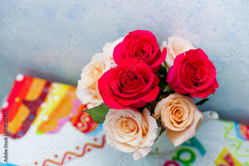 Romantic bouquet of red and creme beige roses as gift to st. Valentine holiday on colorful table and gray background
