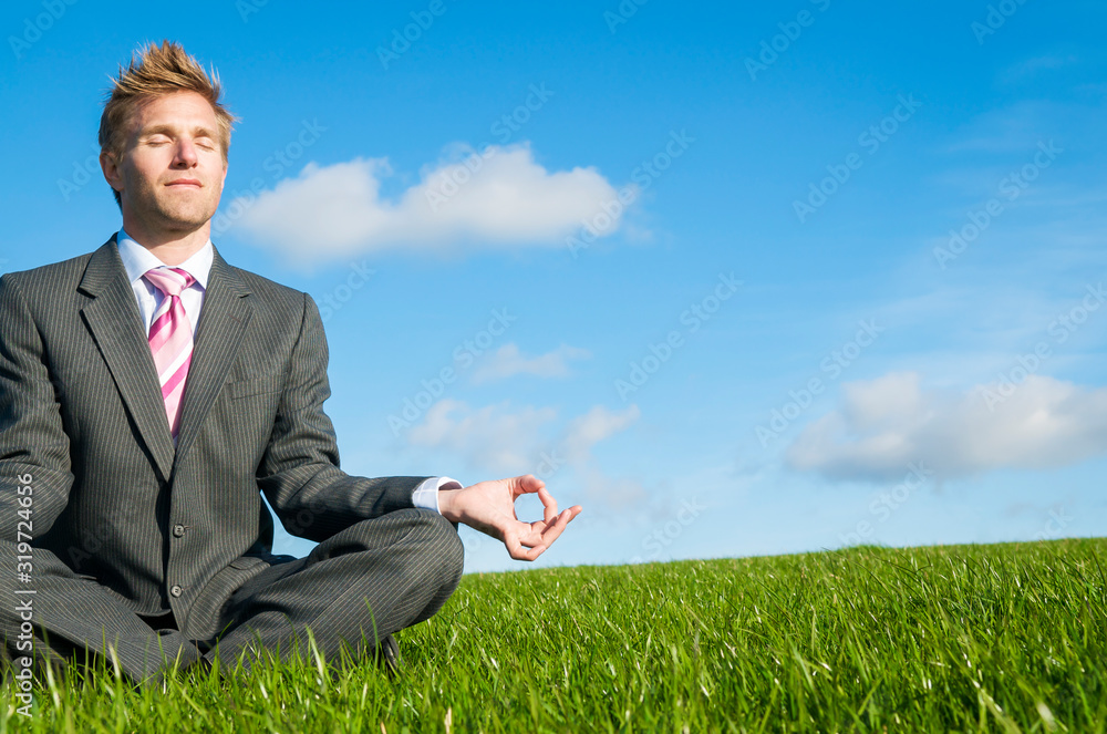 Meditating businessman sitting with eyes closed in a cross-legged yoga pose outdoors in summery green field Meditating businessman sitting with eyes closed in a cross-legged yoga pose outdoors in summery green field
