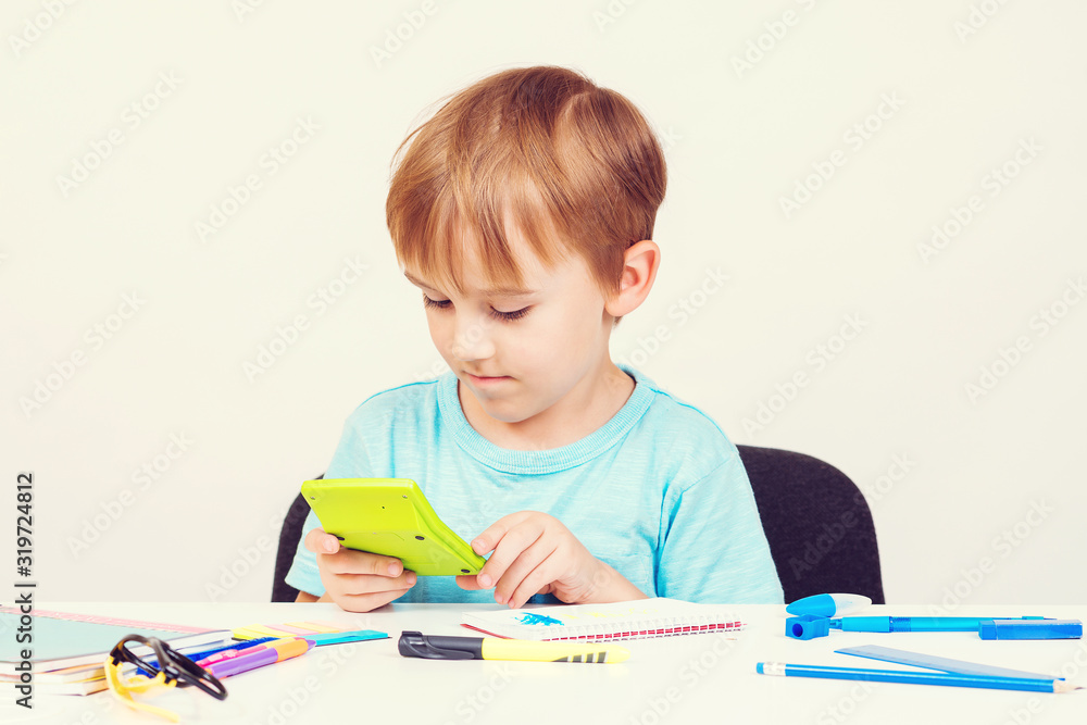 Smart little boy holding calculator. Child doing homework. Back to school concept. School supplies on a white desck. Smart little boy holding calculator. Child doing homework. Back to school concept. School supplies on a white desck.