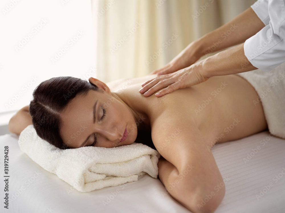 Pretty brunette woman enjoying procedure of back massage in spa salon. Beauty concept