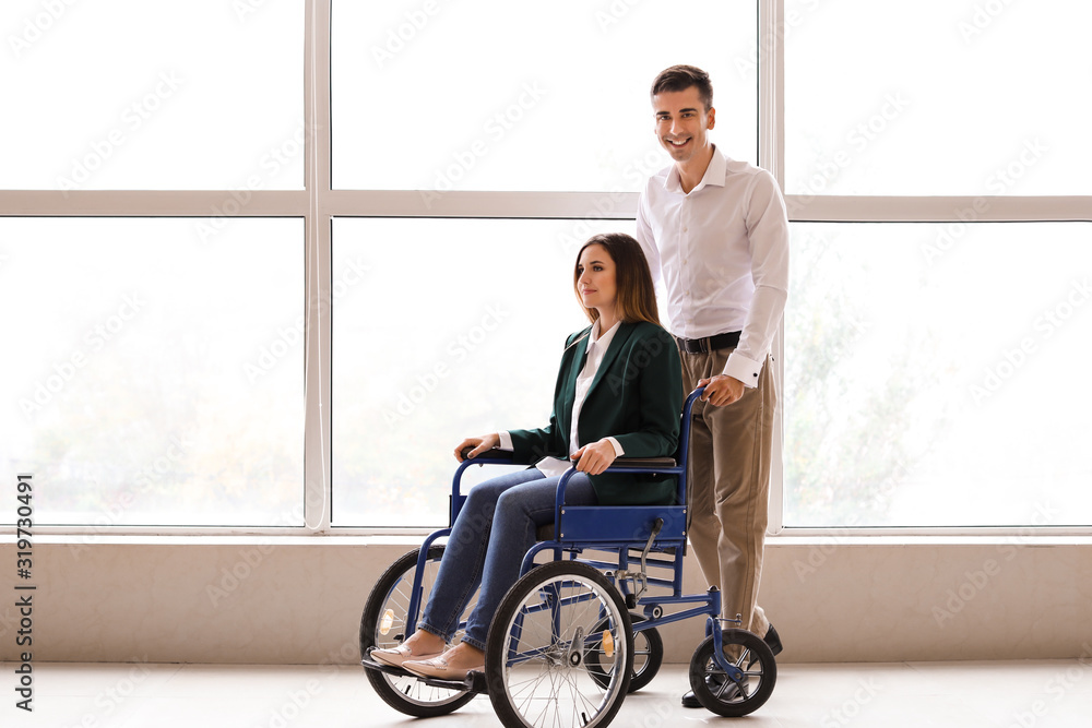 Handicapped young woman in wheelchair and her husband near window Handicapped young woman in wheelchair and her husband near window