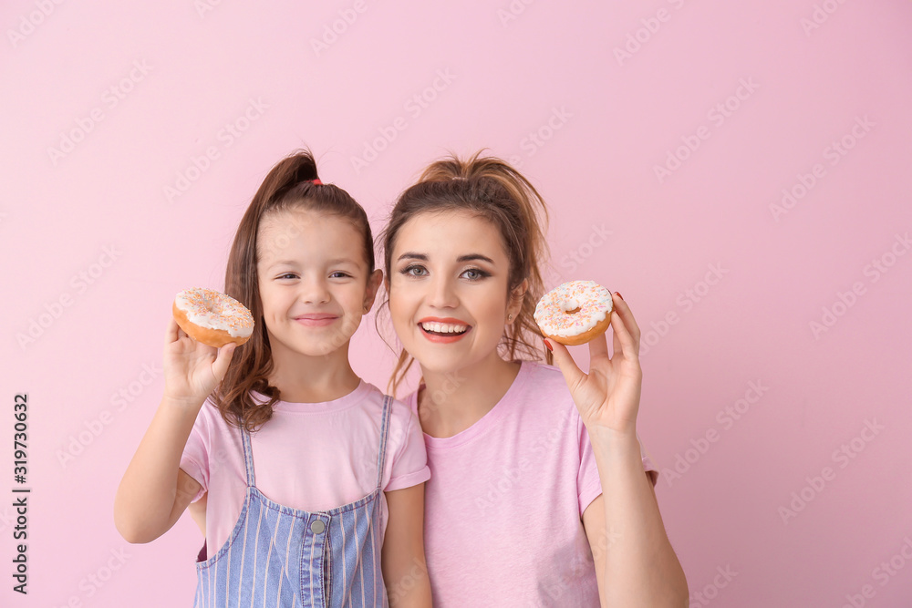 Beautiful young woman and little girl with donuts on color background