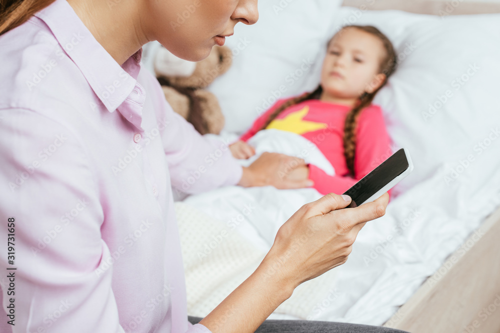 cropped view of mother using smartphone with ill daughter in bed cropped view of mother using smartphone with ill daughter in bed