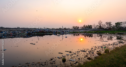 Polluted water and mountain large garbage pile and pollution at the sun is setting in the background