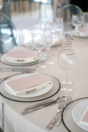 Decor for a luxury gala dinner. Table decorated on white and pink colors. Serving from plates, cutlery and glasses.