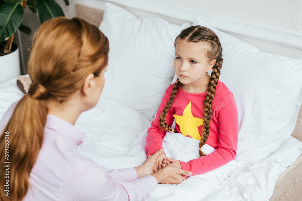 mother holding hands with upset sick daughter in bed mother holding hands with upset sick daughter in bed