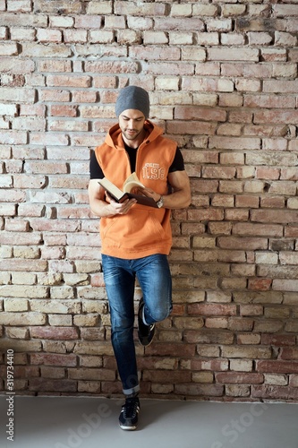 Young man in cap standing at wall reading book