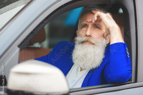 Old handsome man inside the car. Bearded mature male in the automobile. Confident businessman buying the car.