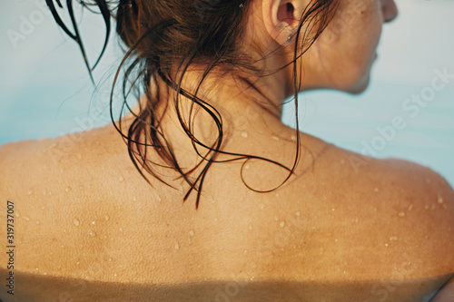 Beautiful young woman relaxing in pool, shoulder with water drops close up. Back view of brunette girl with wet skin with goosebumps. Summer vacation. Enjoying summer holiday, swimming in pool
