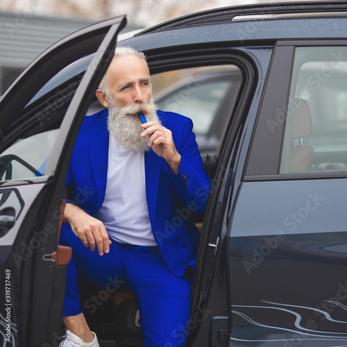 Old styish man standing near the luxury automobile. Mature rich male in the suit outdoors near the car. photo